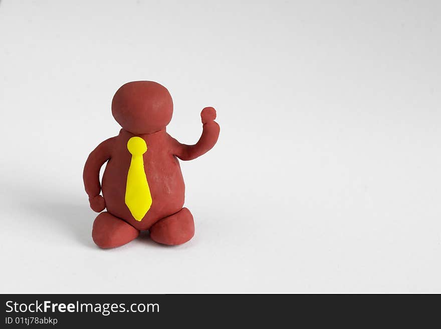 Plasticine man with a yellow tie keeping one hand up over grey background