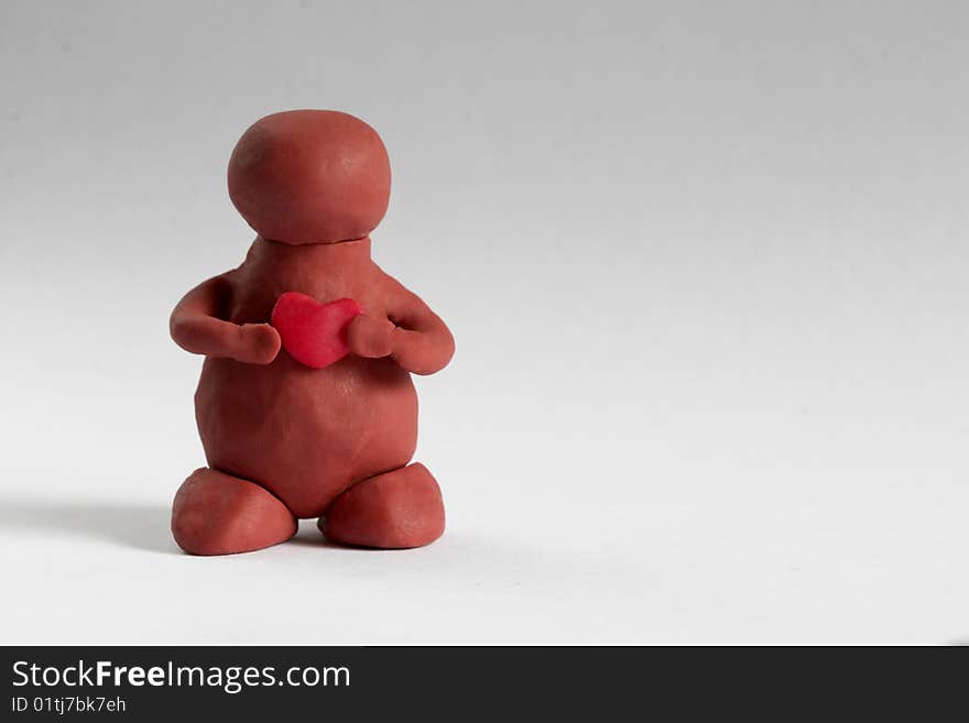 Plasticine man keeping a heart in the hands over grey background