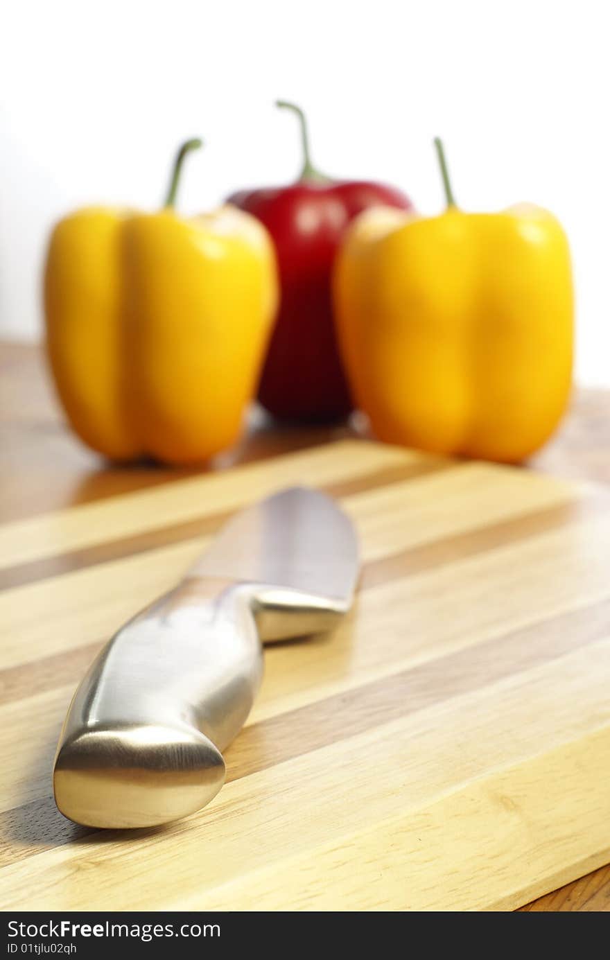 Knife on chopping board and capsicum chilli peppers in the background