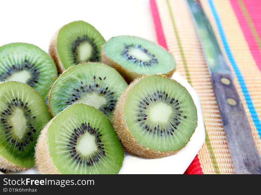 Slices of kiwi on a white plate with a colorful napkin to the side along with a knife. Slices of kiwi on a white plate with a colorful napkin to the side along with a knife.