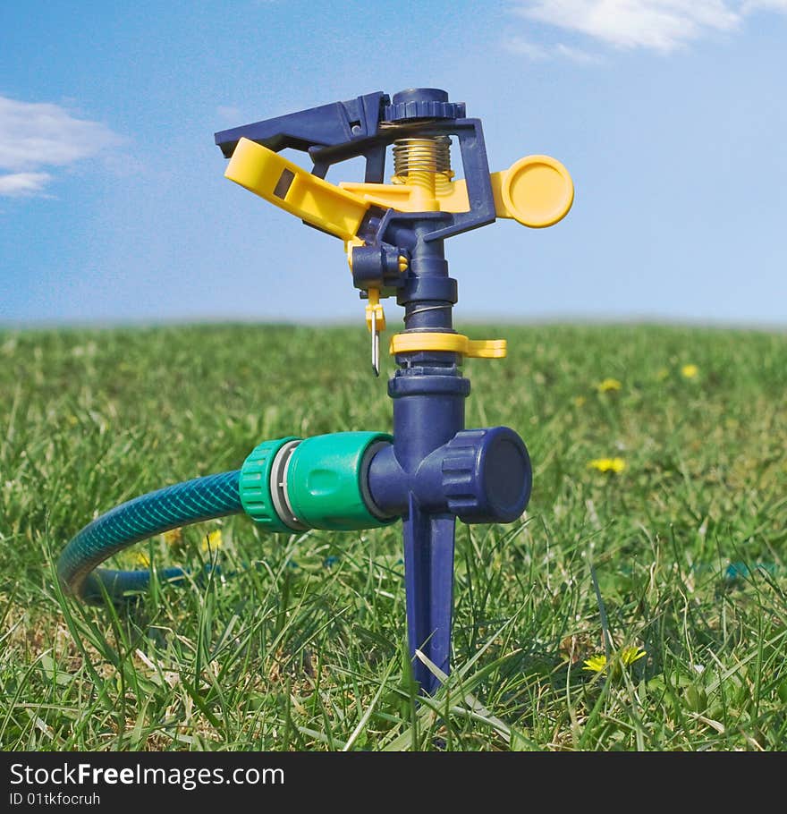 Lawn sprinkler water against the background of grass and sky