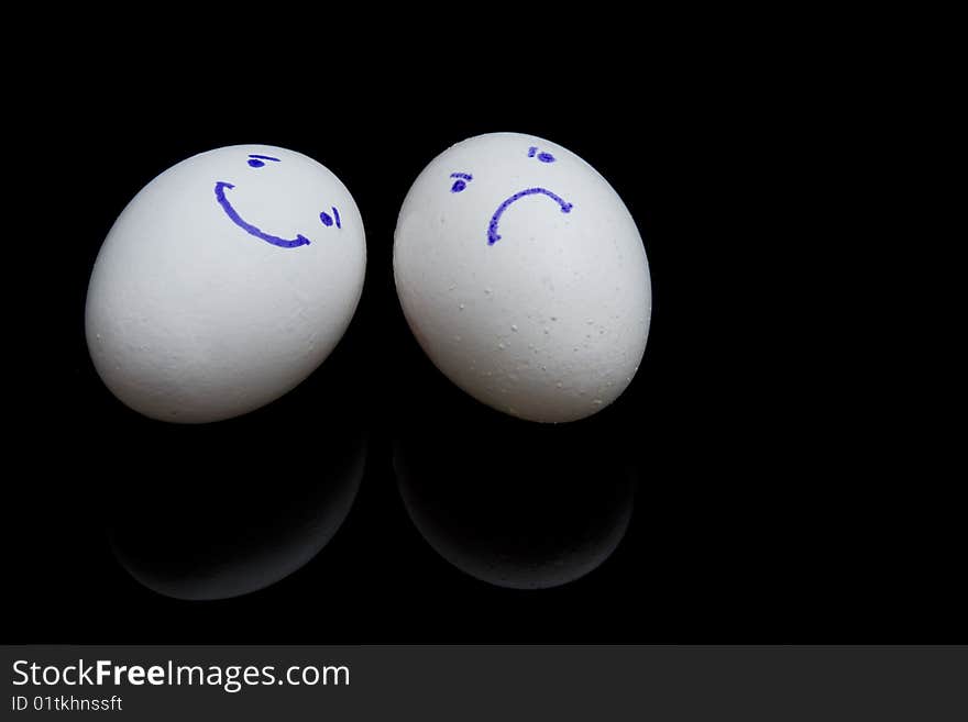 Composition of two white eggs with smiling and sad faces on black background. Composition of two white eggs with smiling and sad faces on black background