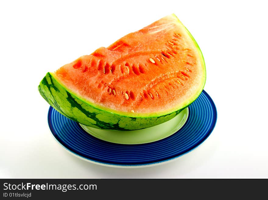 Slice of watermelon with green skin and red melon with seeds on a blue plate with a white background