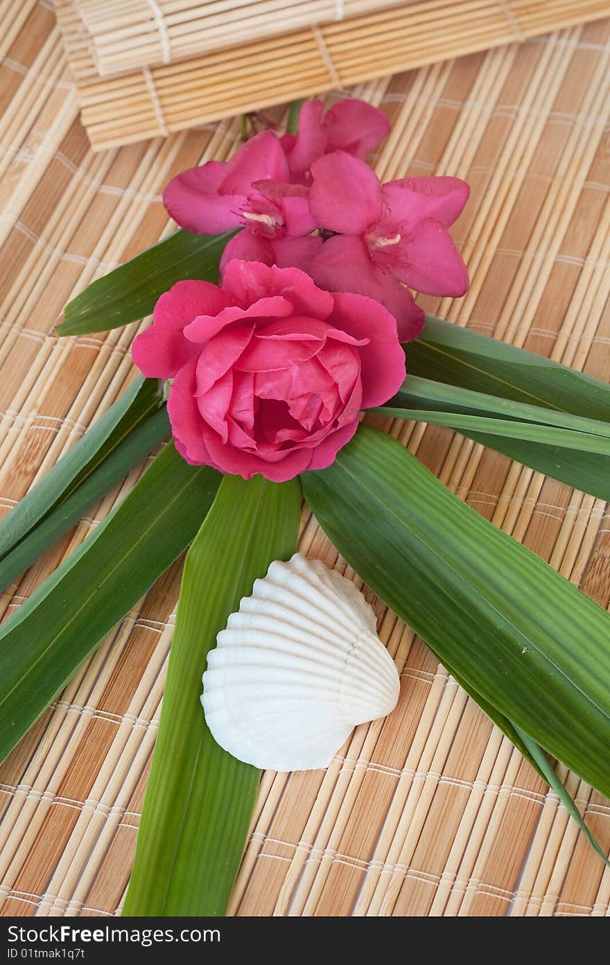 Decoration at the beautiful vacation: rose and oleander flowers set on a bamboo mat with a seashell and bamboo leaves