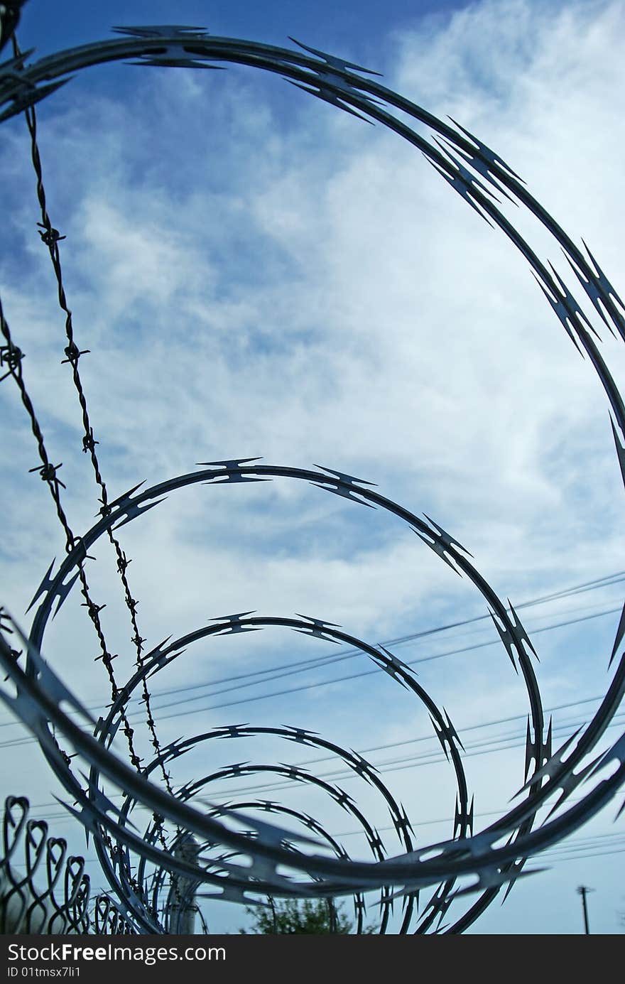 Loops of razor wire and barbed wire protective security fencing on top of a chainlink fence. Loops of razor wire and barbed wire protective security fencing on top of a chainlink fence