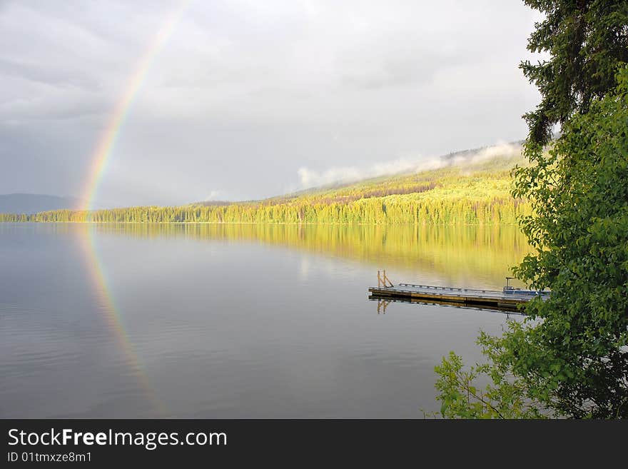 A rainbow forms over a calm forested lake. A rainbow forms over a calm forested lake