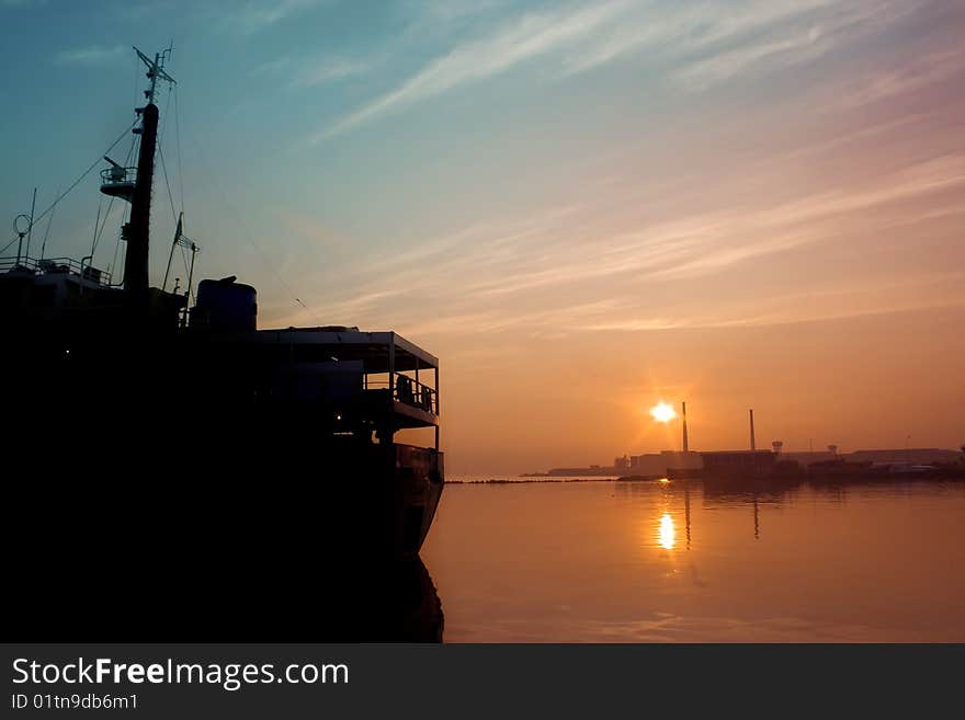 A sillhoutte of cargo ship docking at port, taken early in morning, when red and golden sunrise blending into the blue morning sky. A sillhoutte of cargo ship docking at port, taken early in morning, when red and golden sunrise blending into the blue morning sky