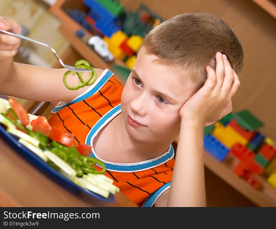The little boy eats fresh salad on the table. The little boy eats fresh salad on the table