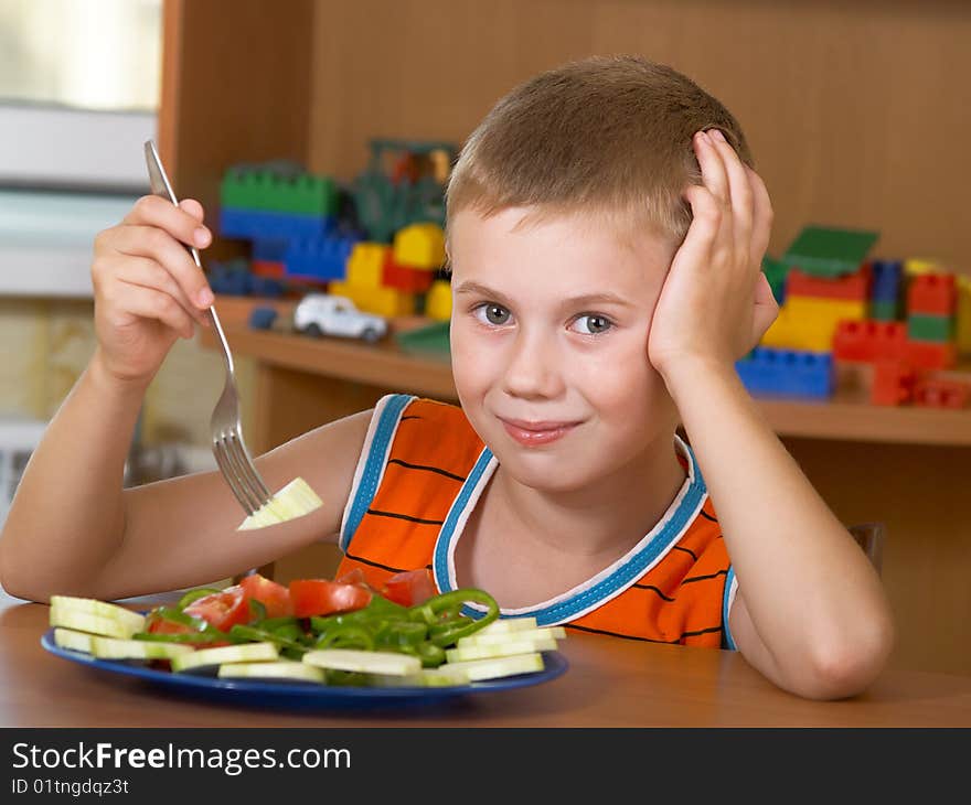 The little boy eats fresh salad on the table. The little boy eats fresh salad on the table