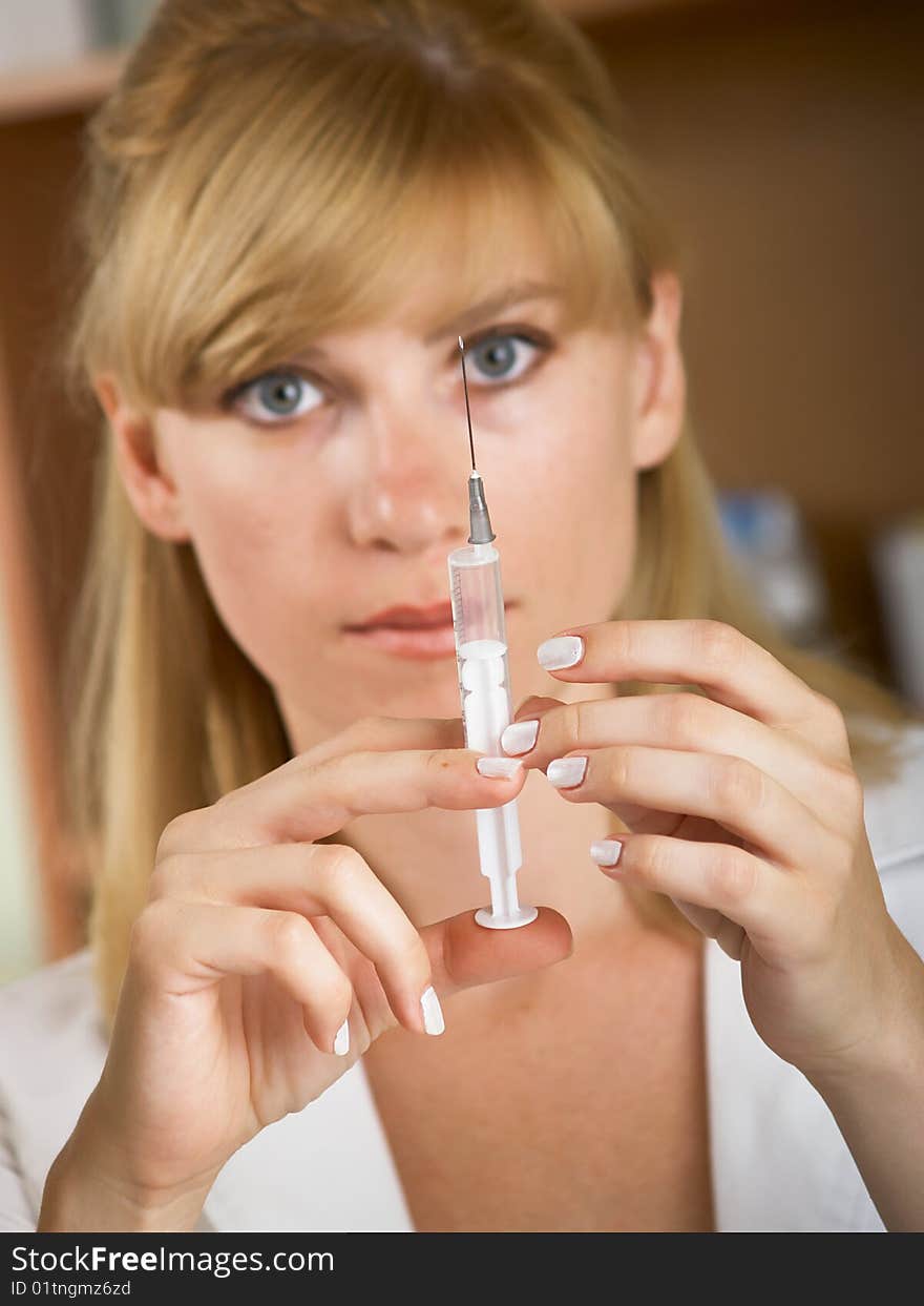 Closeup portrait of beautiful young female doctor looks at a syringe. Closeup portrait of beautiful young female doctor looks at a syringe