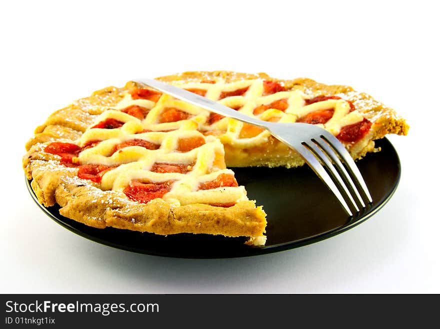 Whole apple and strawberry pie with a small fork on a black plate with a slice missing on a white background. Whole apple and strawberry pie with a small fork on a black plate with a slice missing on a white background