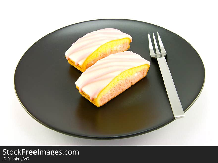 Two pink strawberry sliced cakes with icing on the top with a small fork on a black plate with a white background. Two pink strawberry sliced cakes with icing on the top with a small fork on a black plate with a white background