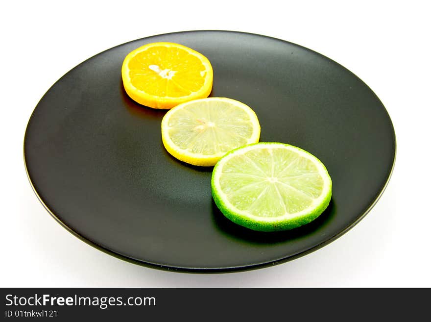 Lemon, lime and orange slices in a line on a black plate on a white background. Lemon, lime and orange slices in a line on a black plate on a white background
