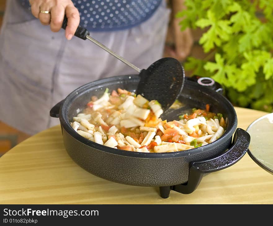 Woman cooking paella. This is the first step: Saute the squids with the vegetables.