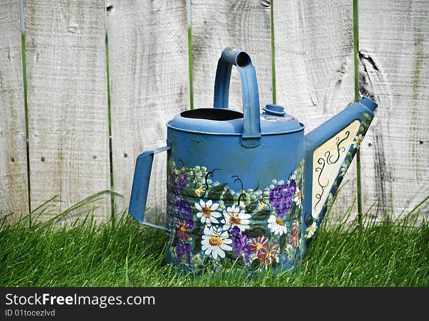 Decorative watering can by an old fence. Decorative watering can by an old fence.