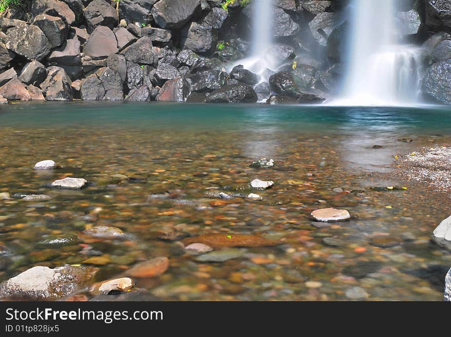 Low shot of majestic waterfall into pool of pebbles