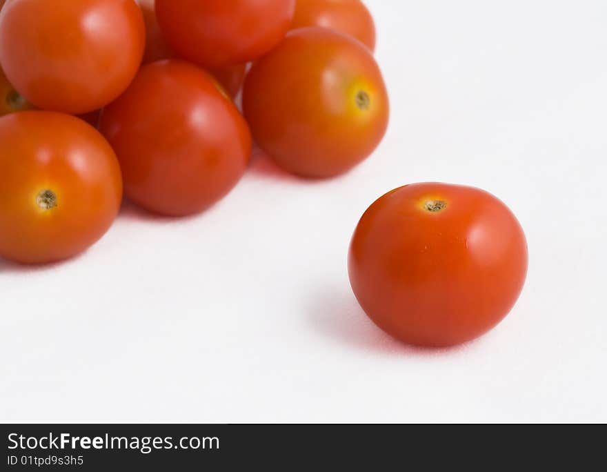 A single cherry tomato in front of a pile of other cherry tomatoes on a white background