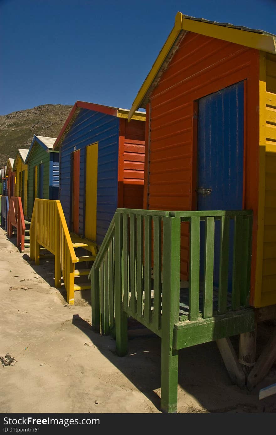 Brightly colored beach huts  standing in a long line on a beach. Brightly colored beach huts  standing in a long line on a beach