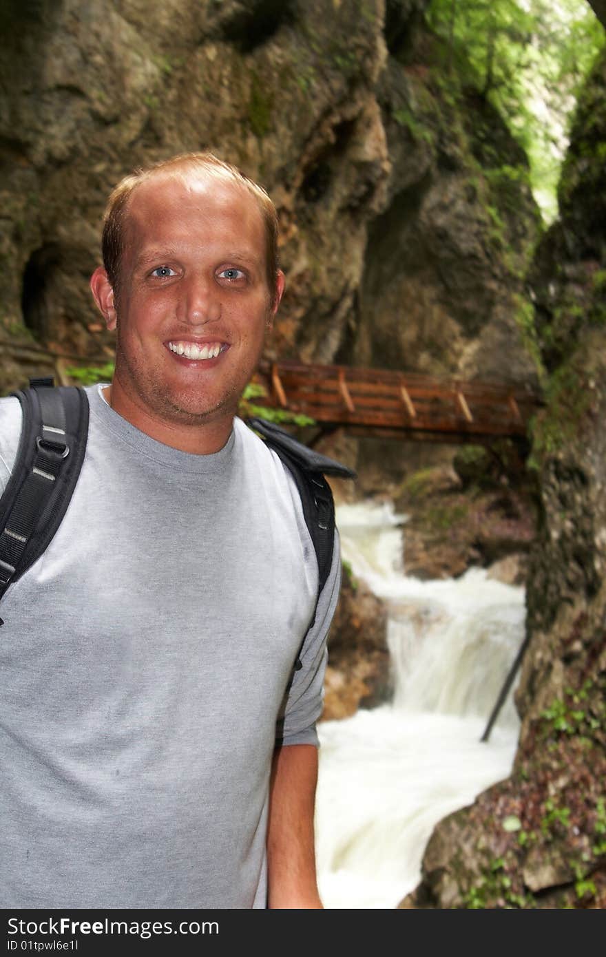 Young man is hiking on a trail in the mountains. A big waterfall in the background - focus on the young man. Young man is hiking on a trail in the mountains. A big waterfall in the background - focus on the young man.