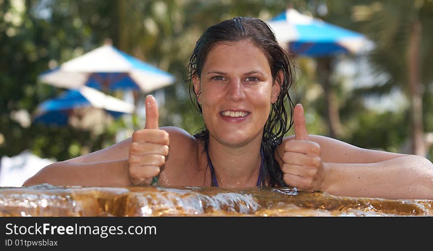 Young woman in a beautiful pool with palms in the background. She is showing a thumbs up sign. Young woman in a beautiful pool with palms in the background. She is showing a thumbs up sign.