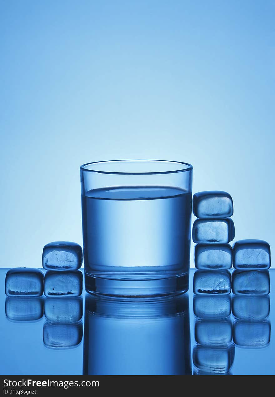 Glass of water and ice cubes on blue background