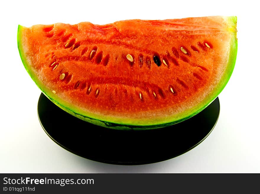 Slice of watermelon with green skin and red melon with seeds on a black plate with a white background. Slice of watermelon with green skin and red melon with seeds on a black plate with a white background