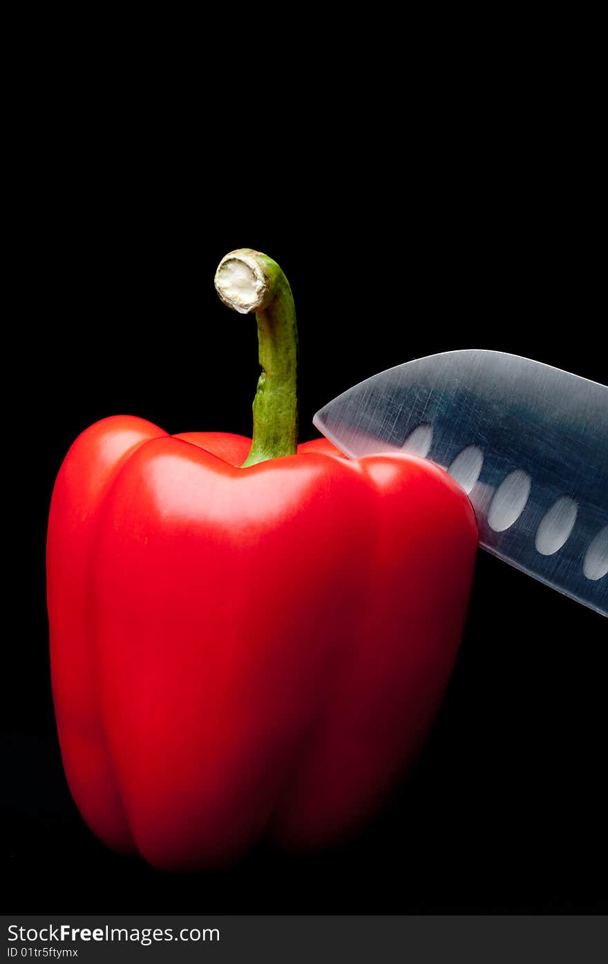 A red pepper being sliced on a dark background