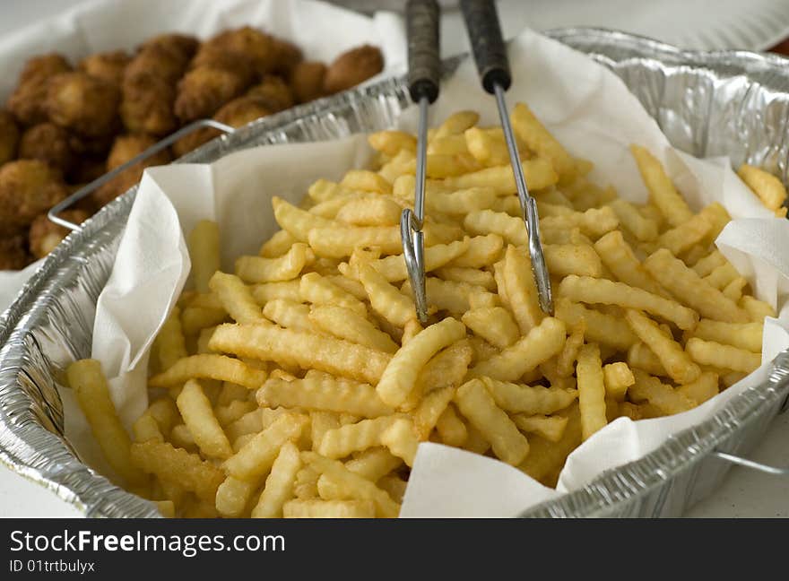 A large pan of deep fried golden brown french fries ready for serving, horizontal with shallow depth of field