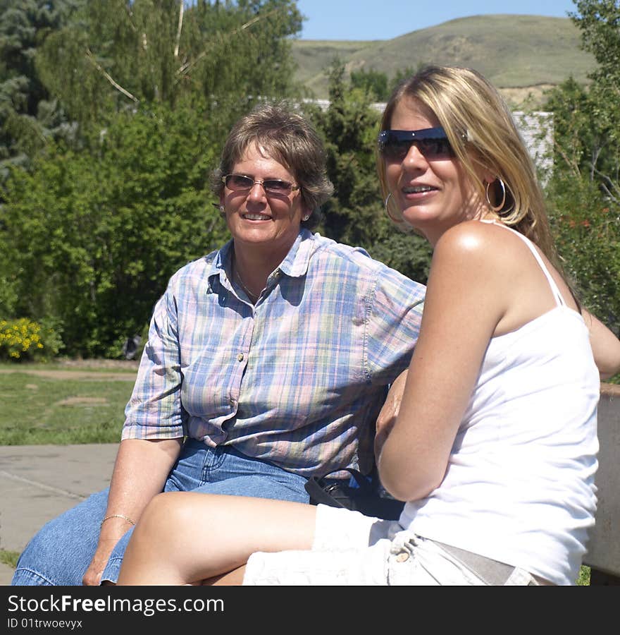 Here is a mother and daughter visiting in the park outside on a sunny day. Here is a mother and daughter visiting in the park outside on a sunny day.