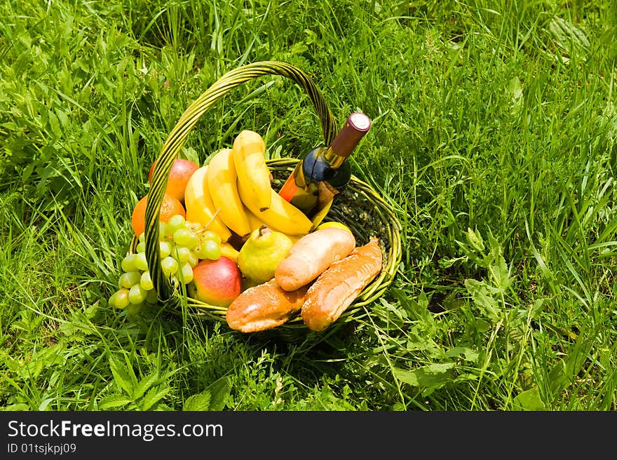 Baking a fruit basket and a bottle of wine on the green grass. Baking a fruit basket and a bottle of wine on the green grass