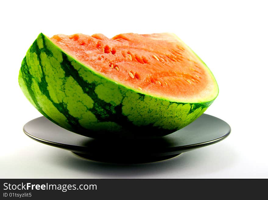 Slice of watermelon with green skin and red melon with seeds on a black plate with a white background. Slice of watermelon with green skin and red melon with seeds on a black plate with a white background