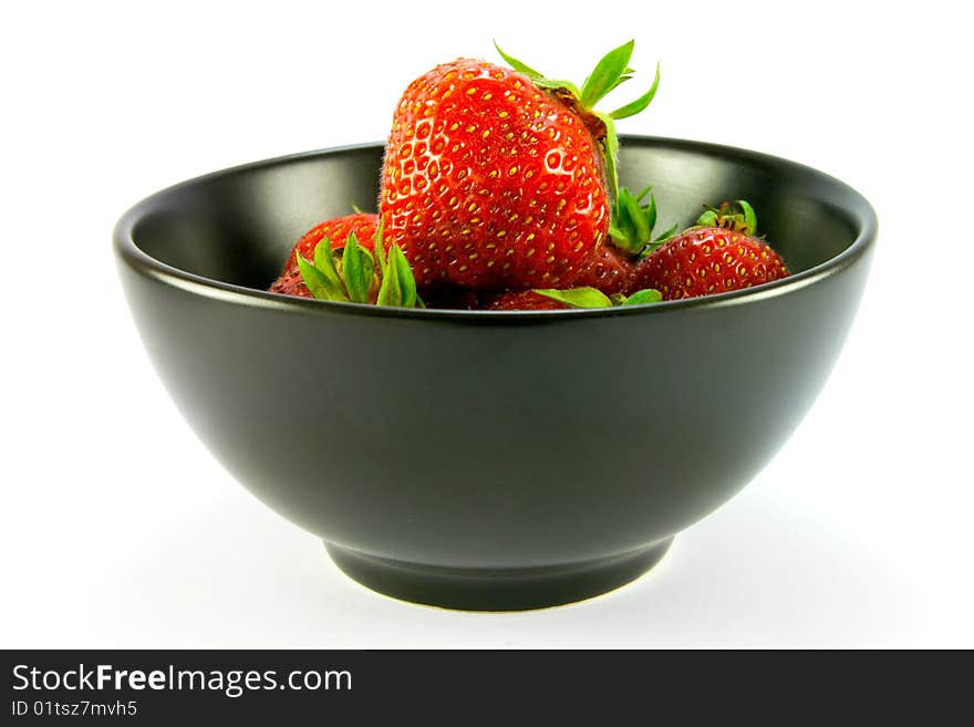 Whole red ripe strawberries in a black bowl on a white background