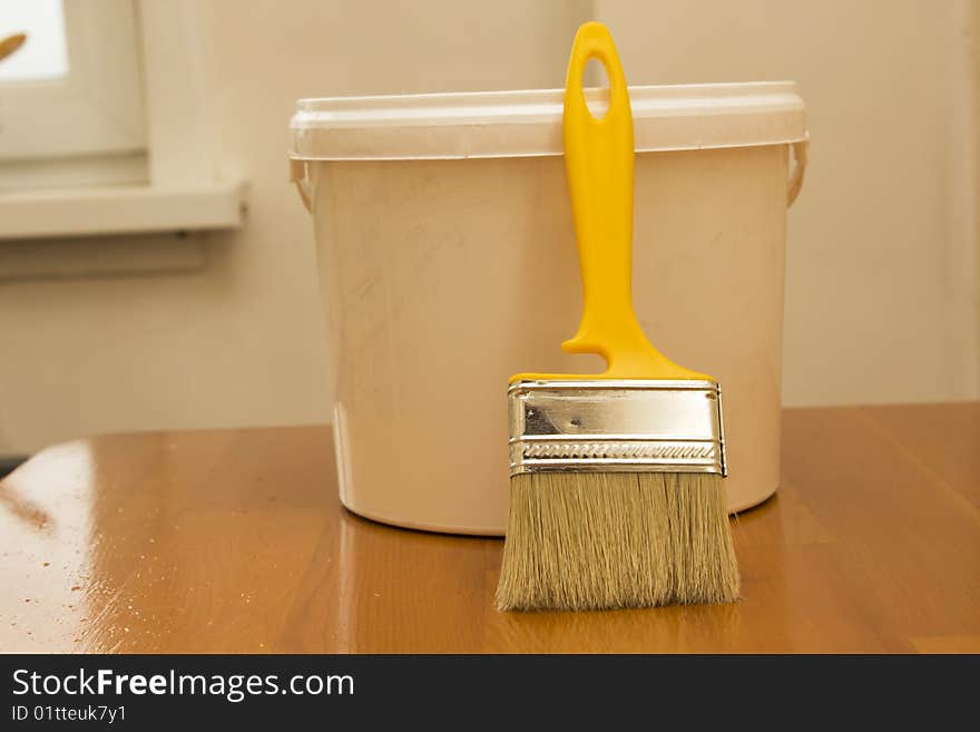 Paintbrush and bucket with paint on wooden table