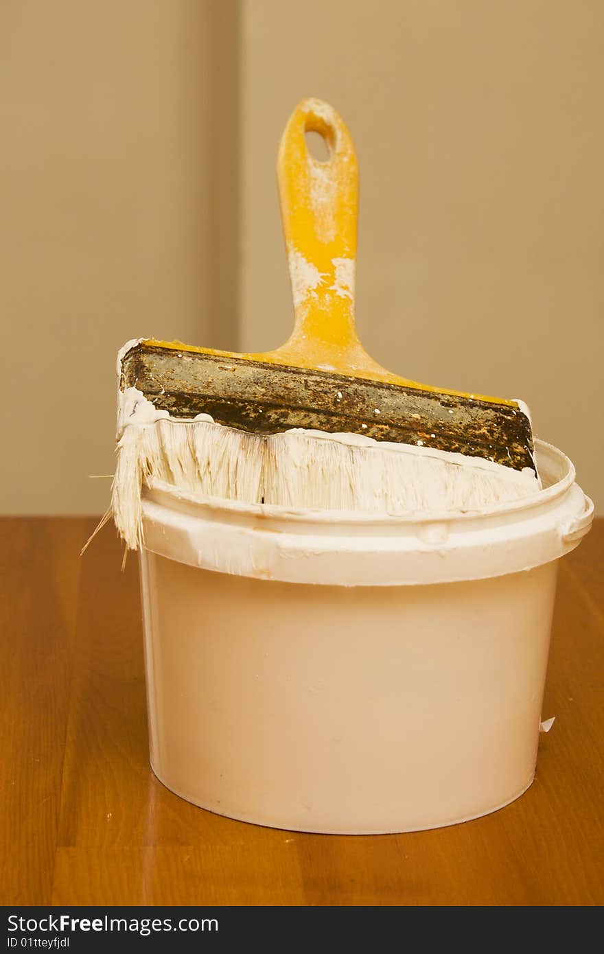 Paintbrush and bucket with paint on wooden table