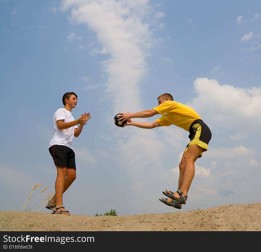 Two boys play a ball on sand