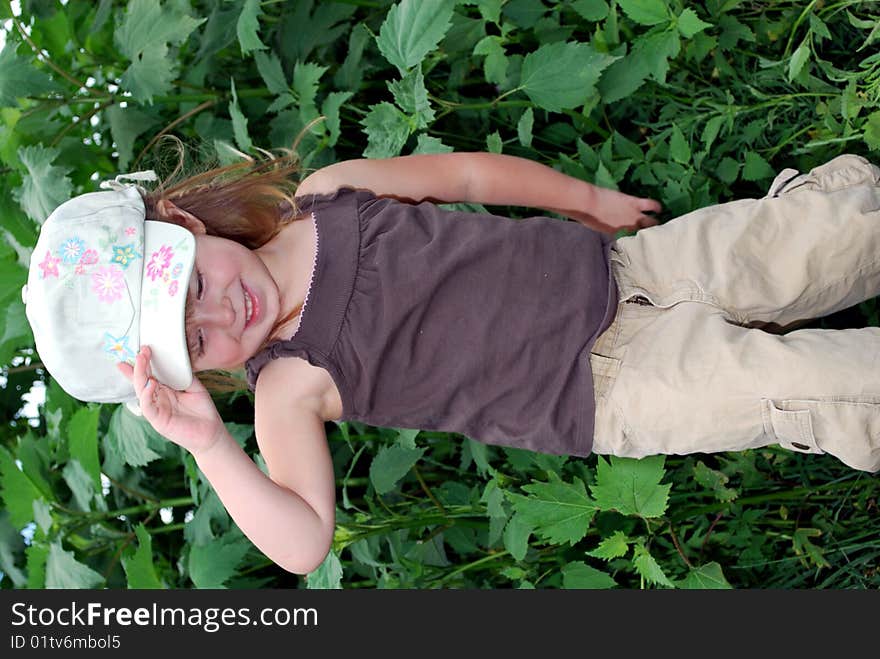 Young girl outside in front of plants with hand on hat posing for camera. Young girl outside in front of plants with hand on hat posing for camera