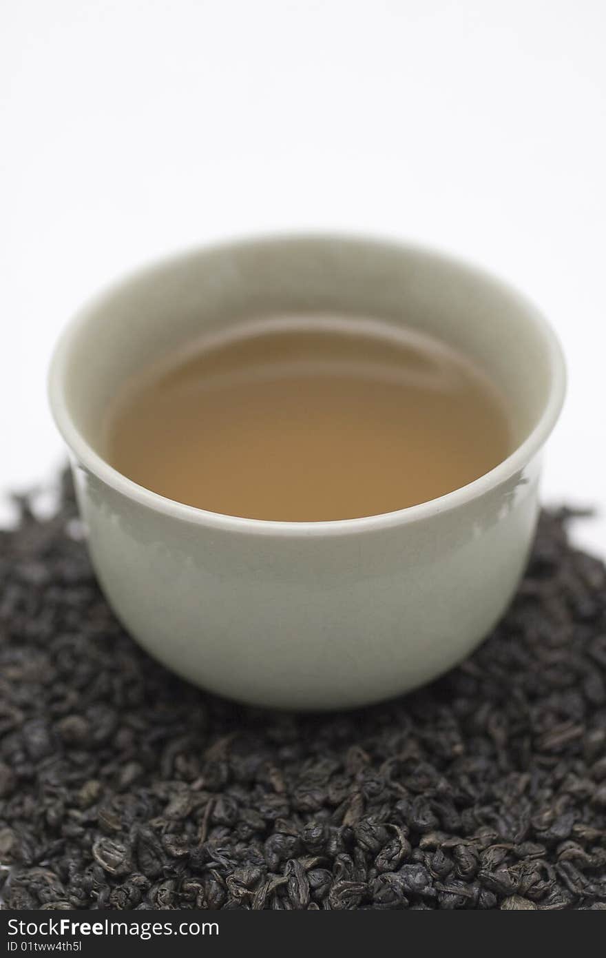 Mug of green tea with tea leaves scattered around