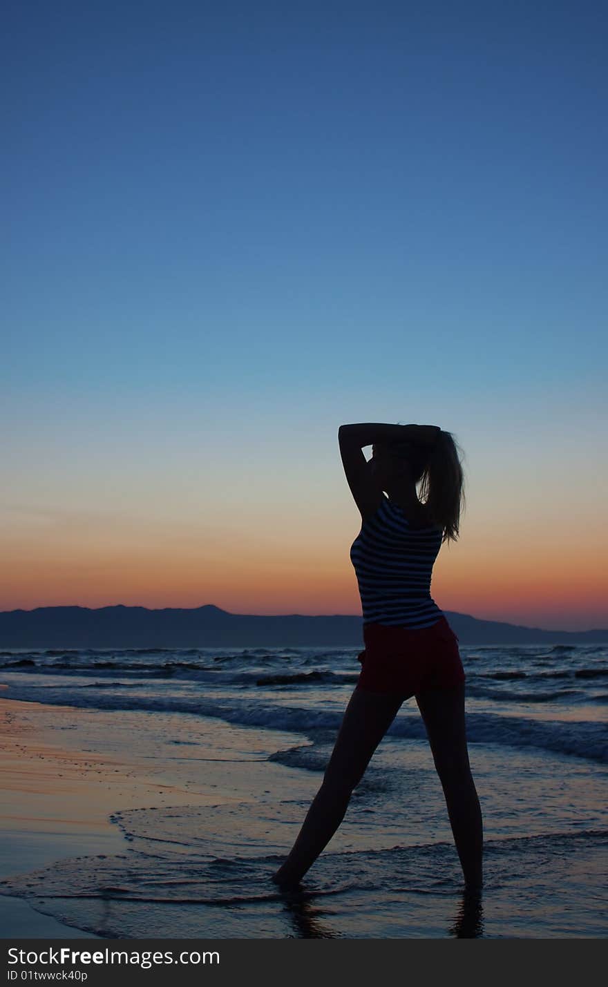 Silhouette of a young woman standing on a beach at sunset. Shot from behind. Silhouette of a young woman standing on a beach at sunset. Shot from behind.