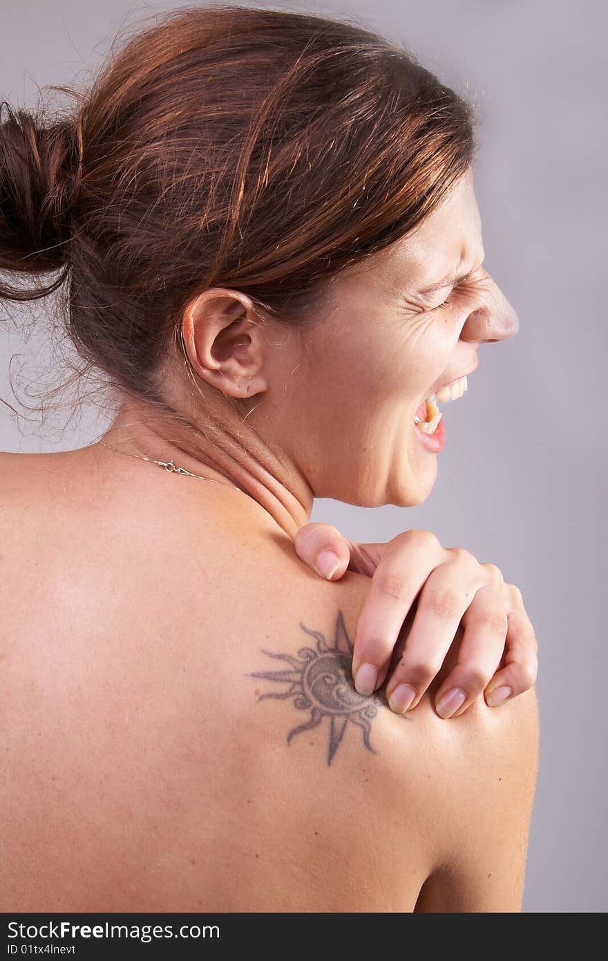 Young woman with sever back pain. She is holding her schoulder. Over grey background. She has a tattoo on her shoulder. Young woman with sever back pain. She is holding her schoulder. Over grey background. She has a tattoo on her shoulder.