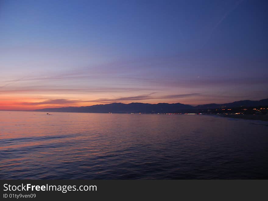 Beautiful sunset on the beach with mountains and city lights