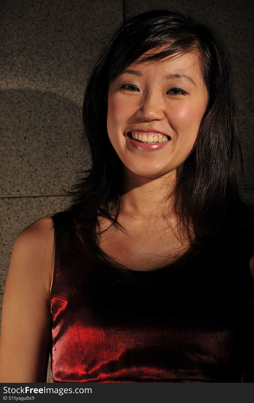 Beautiful young Asian woman in red dress standing against the wall.