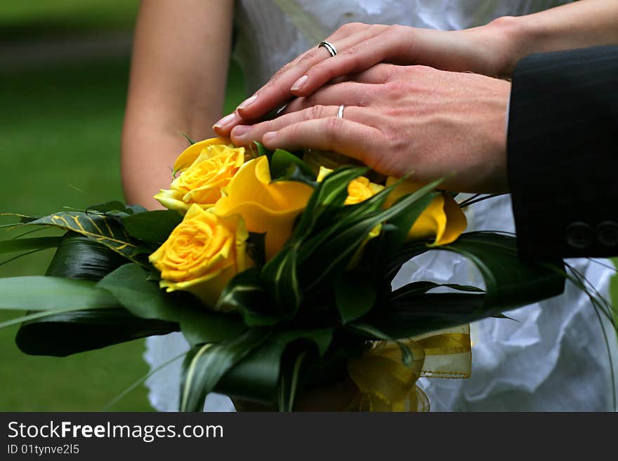 Hands of bride and groom over yellow rose bouquet. Hands of bride and groom over yellow rose bouquet