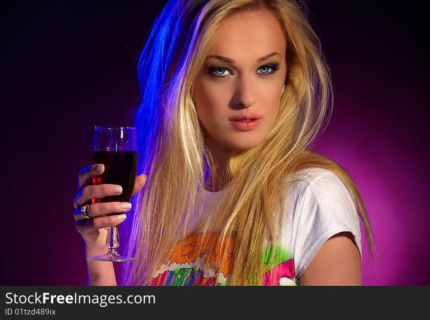 Portrait of a beautiful blonde with green eyes and a glass of wine in their hands on purple background. Portrait of a beautiful blonde with green eyes and a glass of wine in their hands on purple background