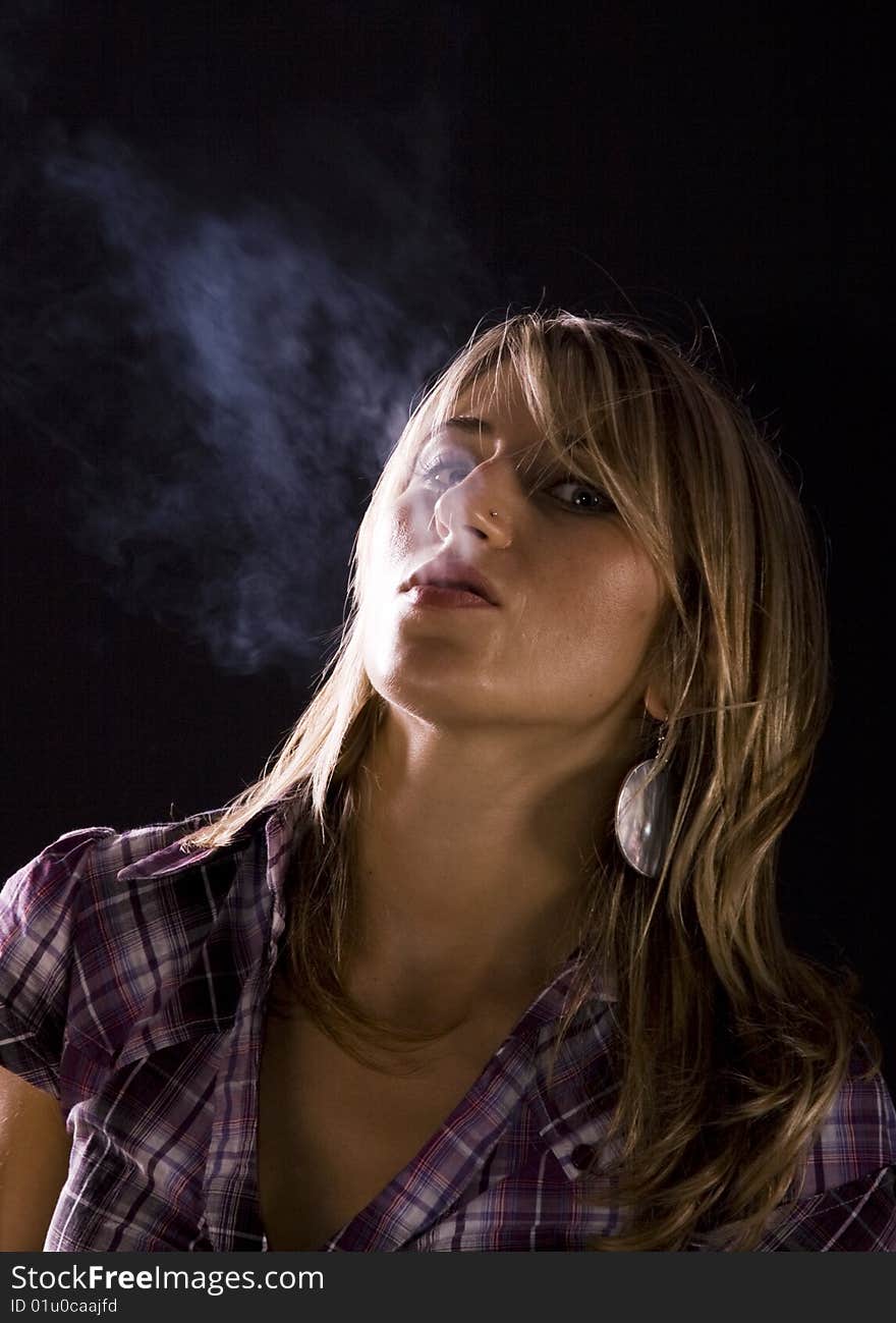 Young woman smoking against dark background