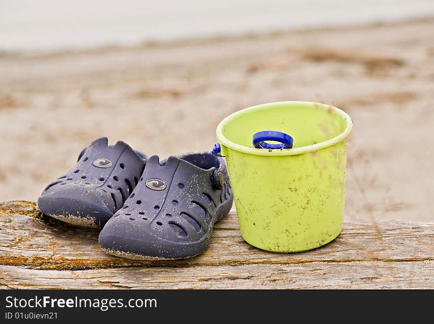 A pair of sandals with a pail on the beach. A pair of sandals with a pail on the beach