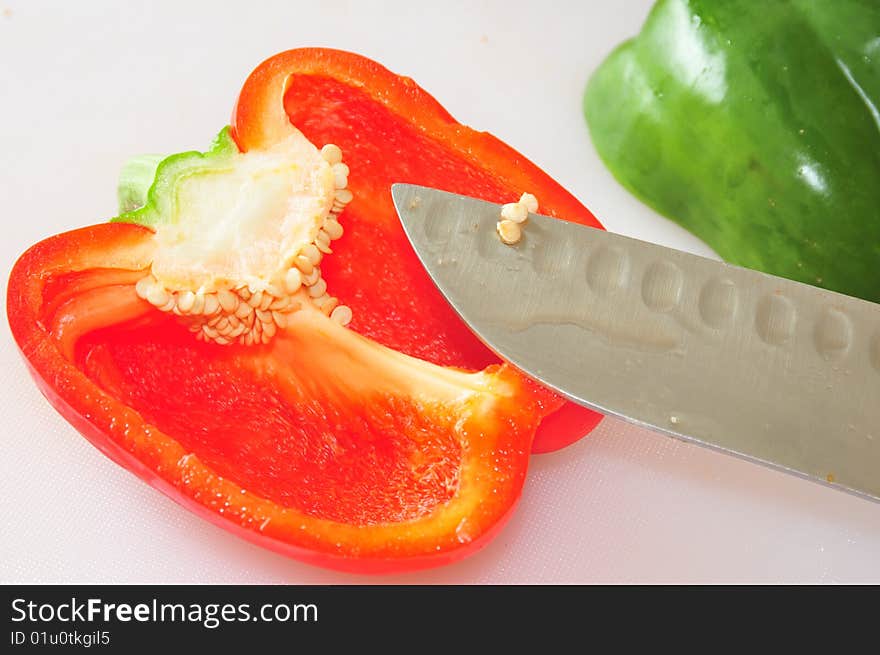 An image of a red bell and a green bell pepper cut in half on a white cutting board. An image of a red bell and a green bell pepper cut in half on a white cutting board.