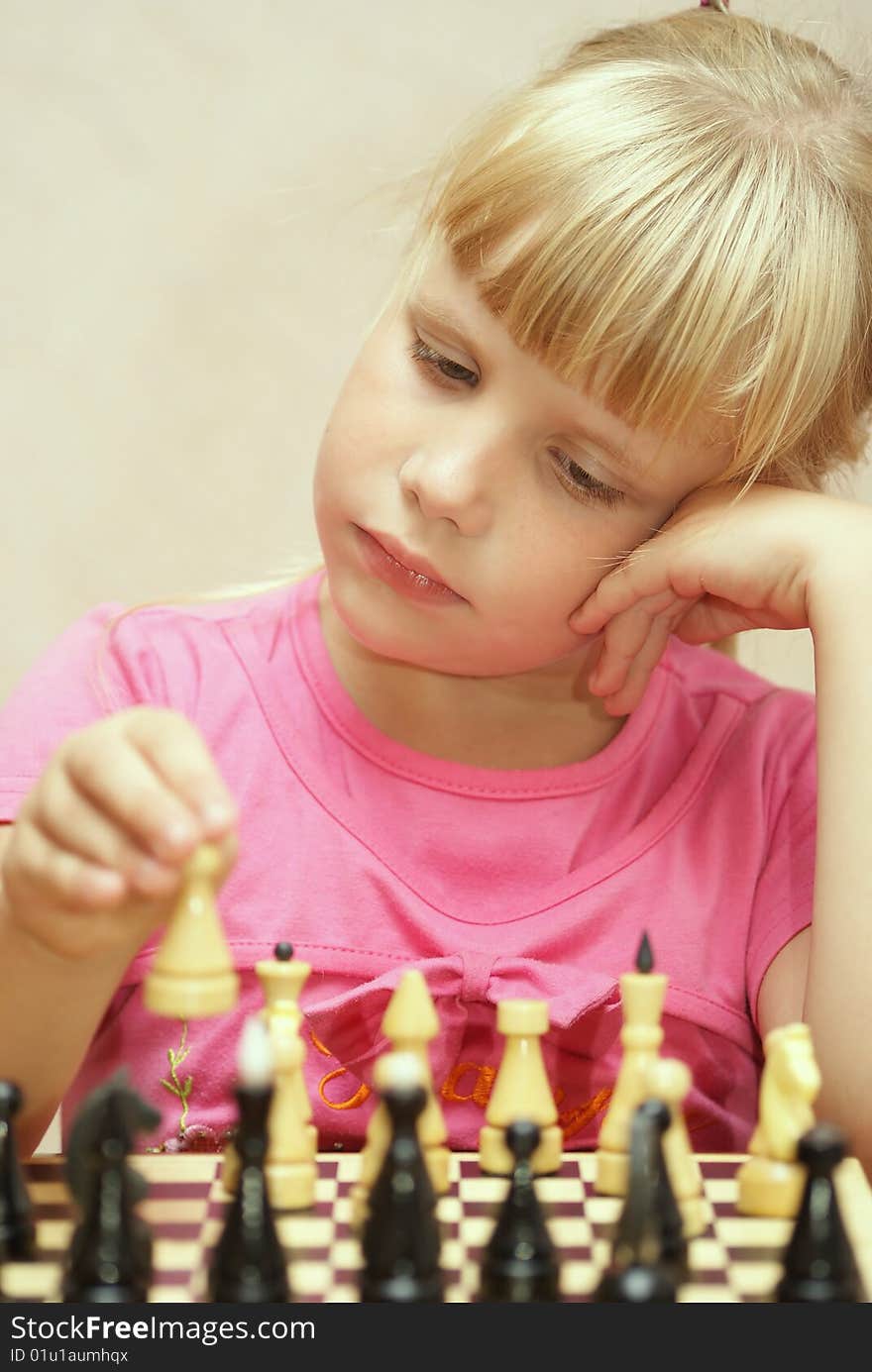 The girl in a pink dress plays a chess