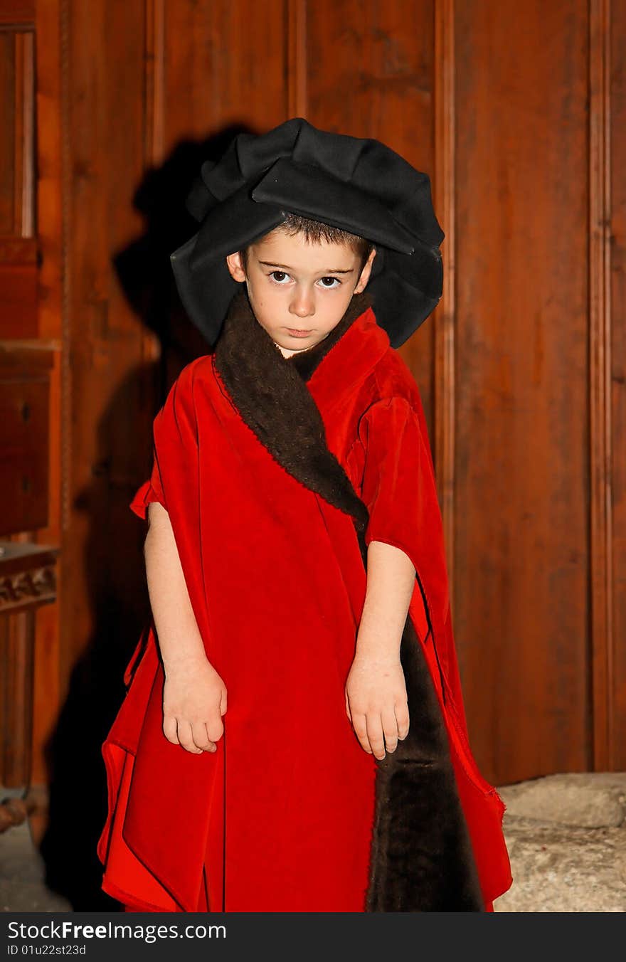 Serious cute little boy in medieval costume standing on wooden background