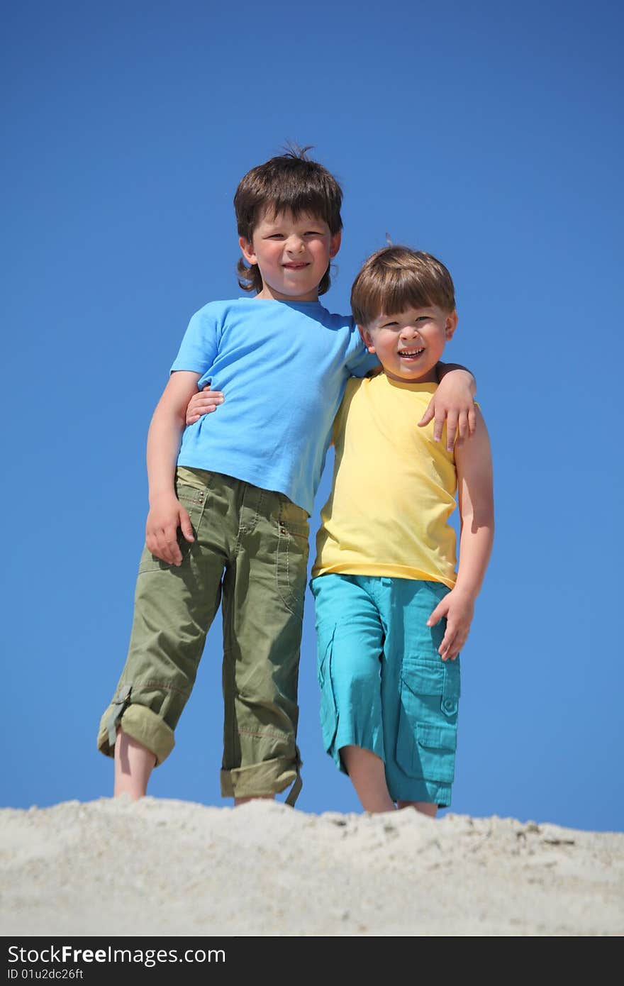 Two boys embrace each other on sand, summer day