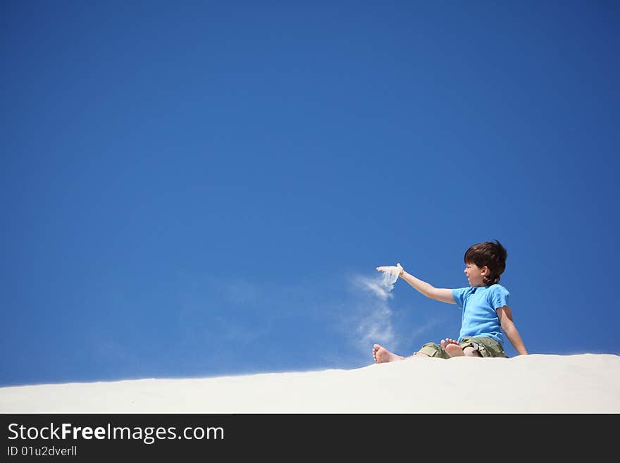 Boy sits on sand and scatters it